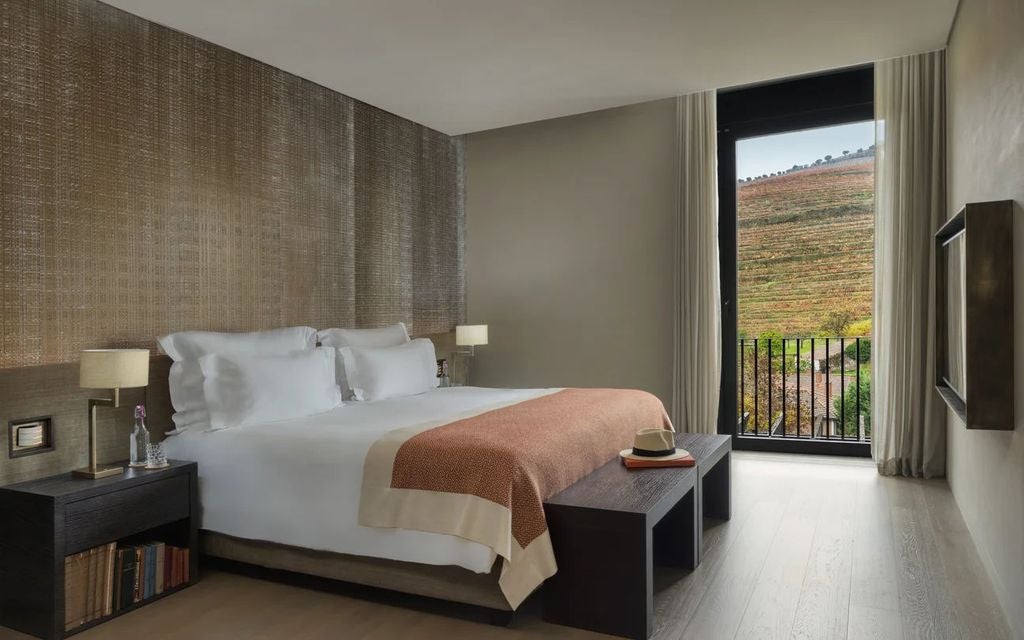 Elegant vineyard suite with floor-to-ceiling windows, modern wood furnishings, and panoramic views of Douro Valley's rolling hills