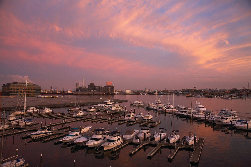 Modern glass high-rise hotel with sleek curved architecture overlooking Baltimore Harbor at sunset, featuring waterfront terraces and infinity pool