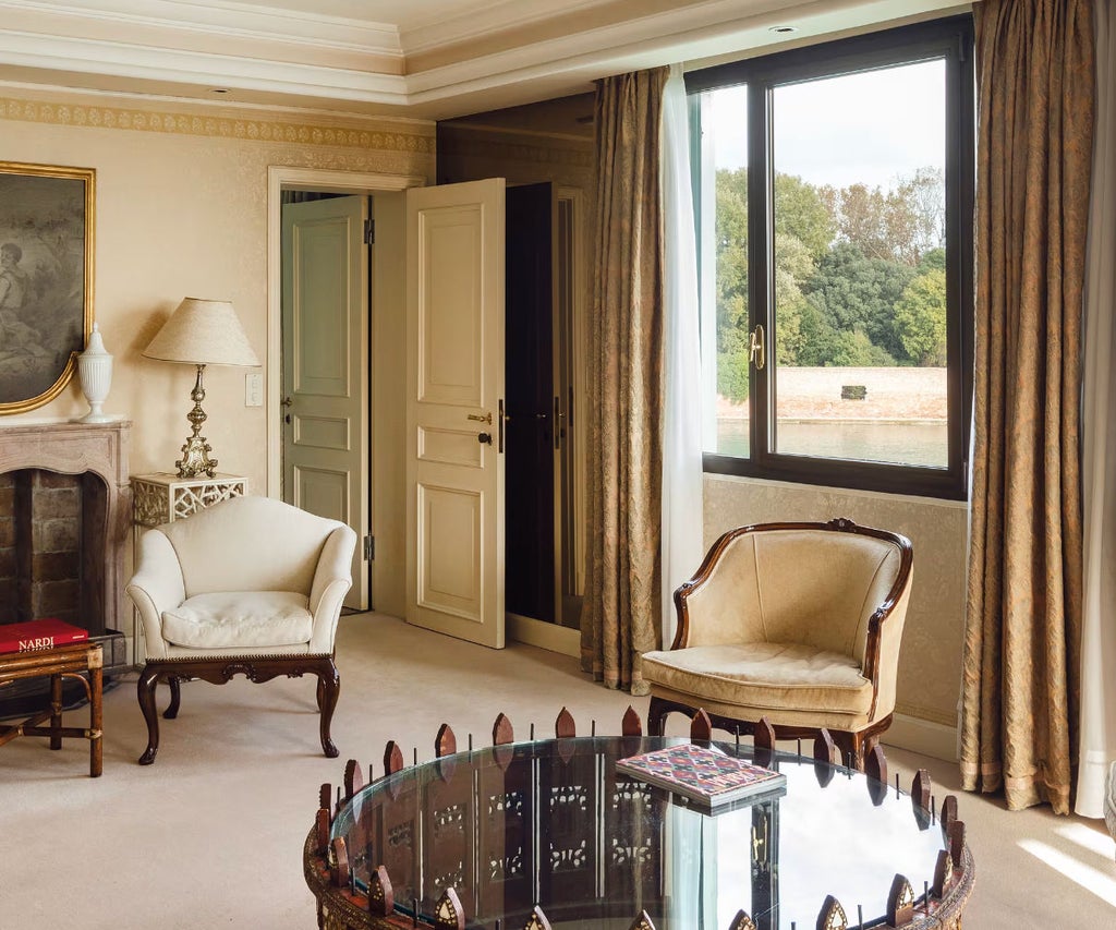 Opulent San Giorgio Suite featuring ornate gold-framed mirror, plush king bed with cream linens, and Venetian lagoon views through arched windows