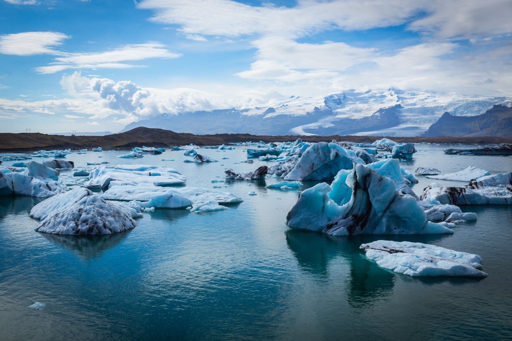 Majestic Icelandic glacier landscape with luminous blue icebergs floating in Jökulsárlón lagoon, surrounded by rugged volcanic terrain of Skaftafell National Park