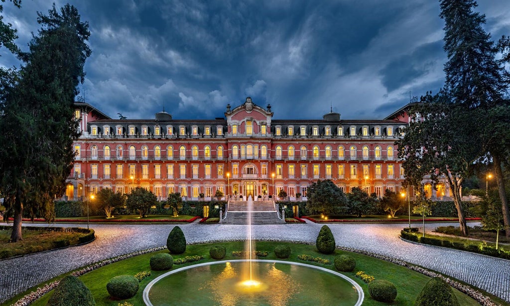 Elegant art nouveau palace hotel with grand white facade, lush green gardens, and ornate architectural details in scenic Portuguese landscape