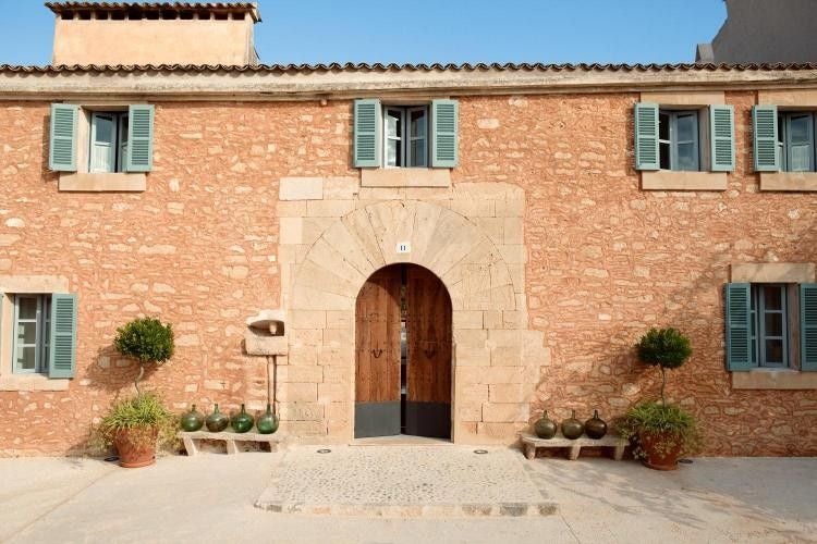 Rustic luxury hotel exterior with stone walls, Mediterranean garden, and mountain views in Mallorca's countryside at sunset