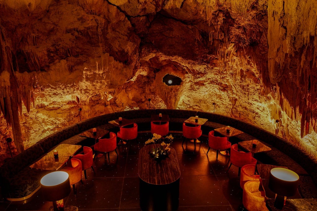 Romantic table setting inside a natural cave with lanterns, white tablecloth, and candlelight overlooking the ocean at sunset