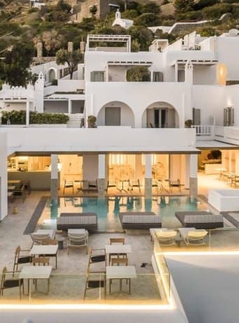 Luxurious white-walled boutique hotel with blue-domed architecture, overlooking Aegean Sea, traditional Cycladic design in scenic Mykonos landscape