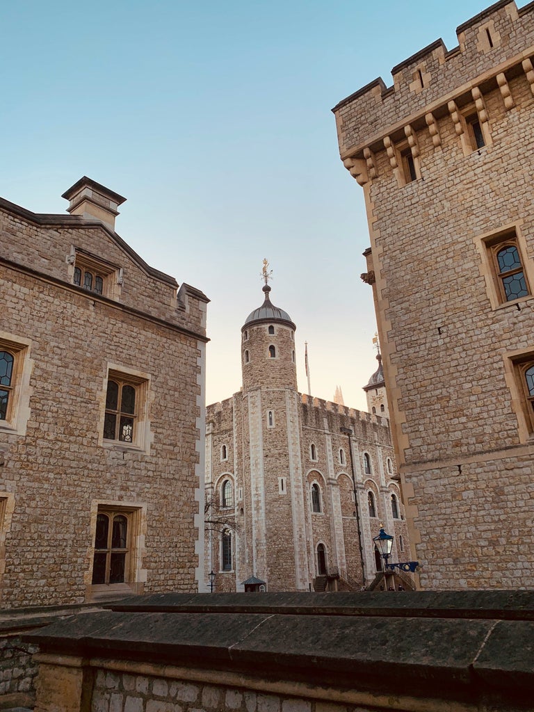 Medieval fortress Tower of London's White Tower rises majestically against cloudy sky, surrounded by ancient stone walls and fortifications