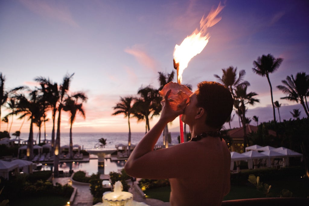 Luxurious oceanfront Four Seasons resort in Maui with infinity pool overlooking Pacific Ocean, surrounded by swaying palm trees at sunset