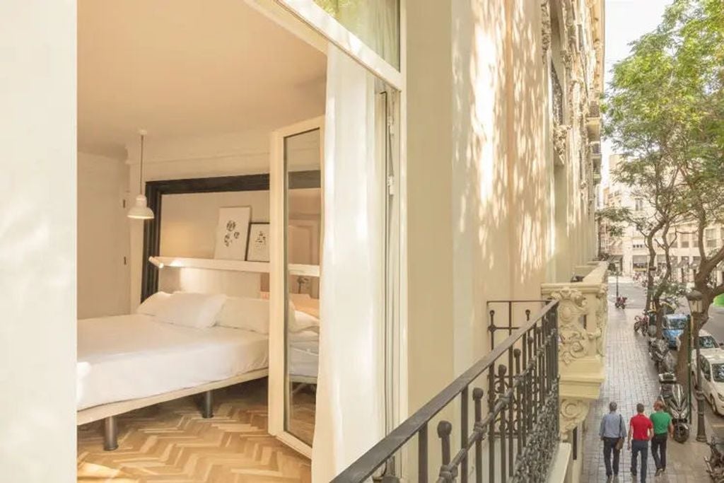 Elegant hotel room with ornate balcony doors overlooking Valencia Palace, featuring classic decor, crisp white bedding and antique furniture.