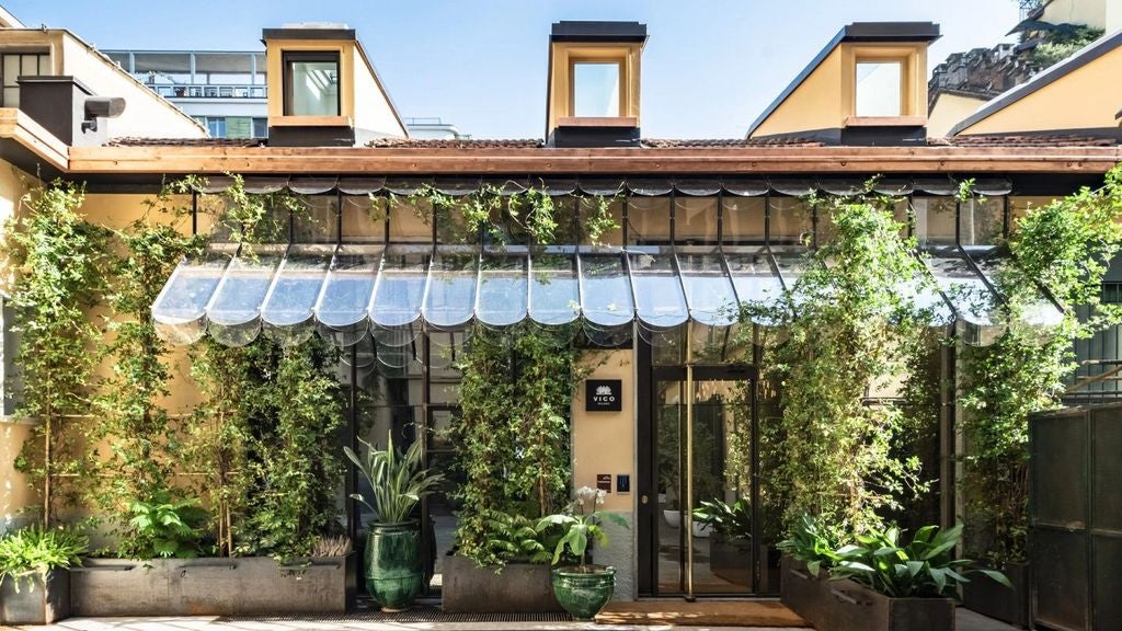 Elegant boutique hotel entrance with ornate stone archway, classic Milanese architecture and warm lighting in upscale city se