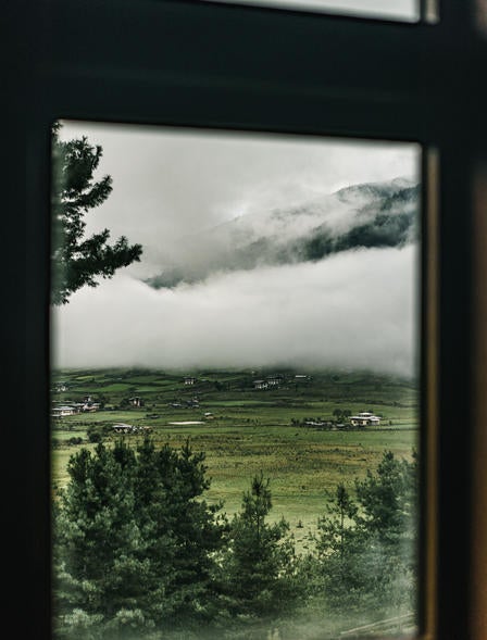 Luxurious mountain lodge nestled in Bhutanese valley, featuring floor-to-ceiling windows with panoramic views of misty Himalayas at sunrise