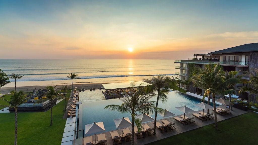 Contemporary beachfront hotel in Bali with sleek infinity pools overlooking the ocean, featuring minimalist architecture and palm-lined walkways