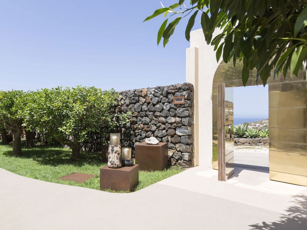 Luxurious boutique hotel with stone walls, elegant terrace overlooking Pantelleria's volcanic landscape, warm Mediterranean sunlight casting golden hues