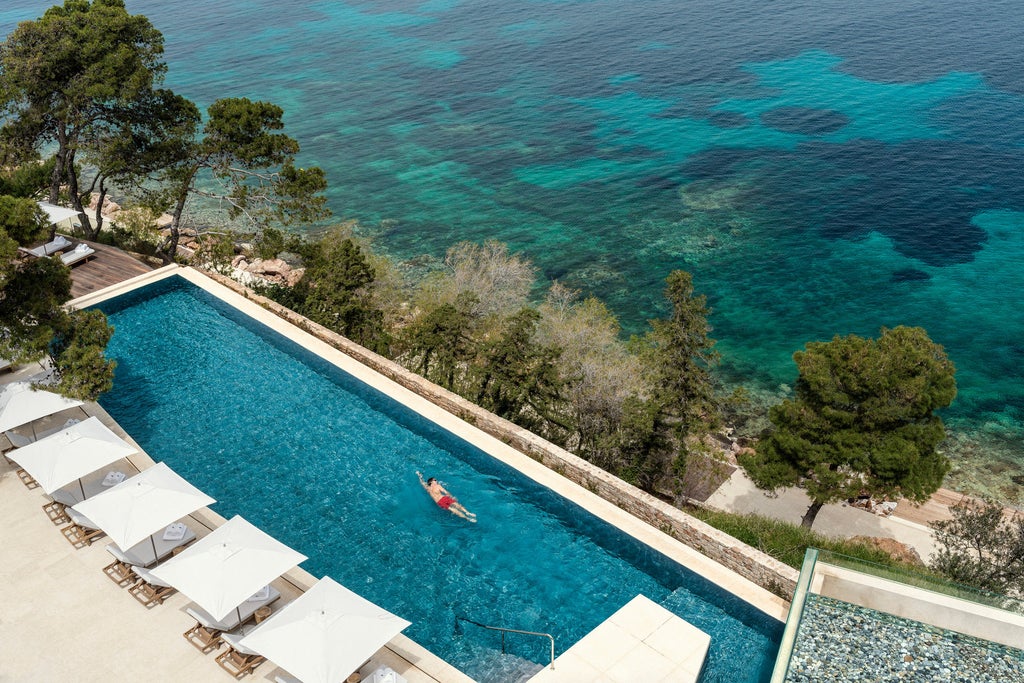 Seaside luxury hotel in Athens with infinity pools overlooking the Aegean Sea, framed by manicured gardens and palm trees at sunset