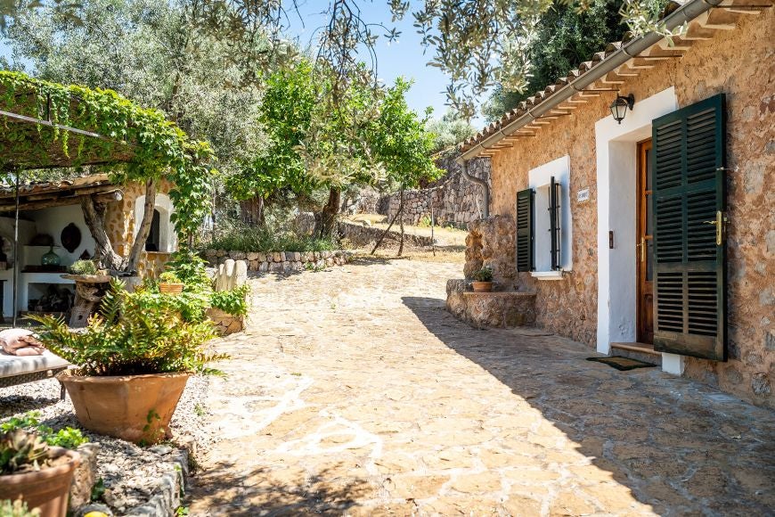 Elegant stone garden cottage at Ca's Xorc Luxury Retreat, featuring lush Mediterranean greenery and rustic Mediterranean architectural charm in Spain