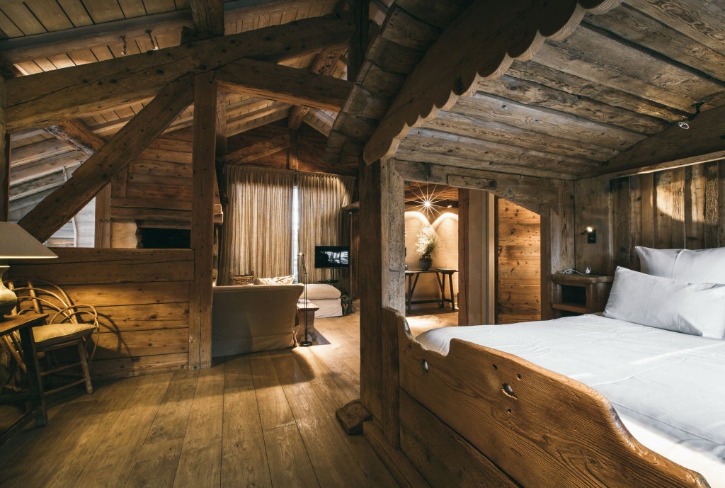 Luxurious alpine suite with warm wooden interiors, plush king bed, panoramic mountain view, and elegant French chalet design in soft neutral tones