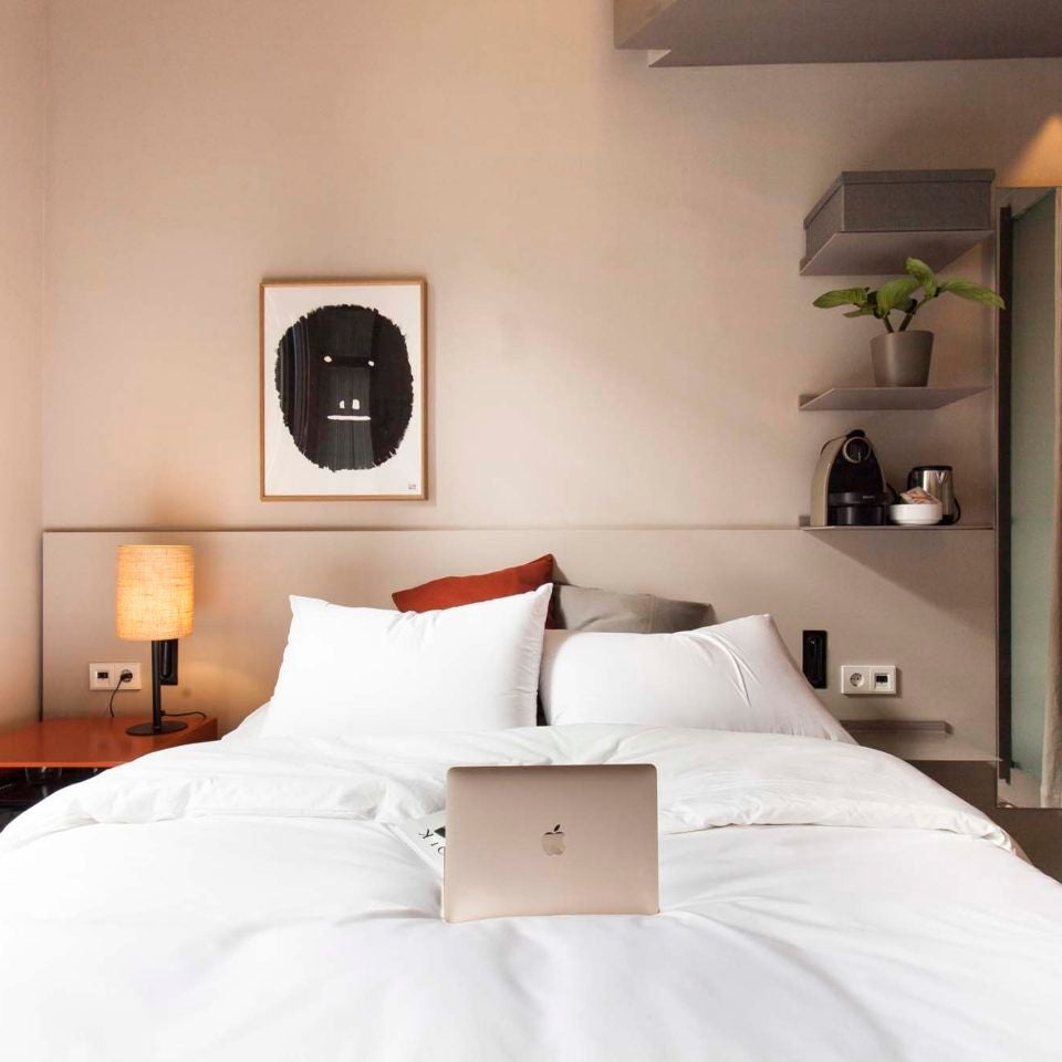 Spacious modern Barcelona hotel room with minimalist design, white walls, wooden floors, and elegant king-sized bed with crisp white linens