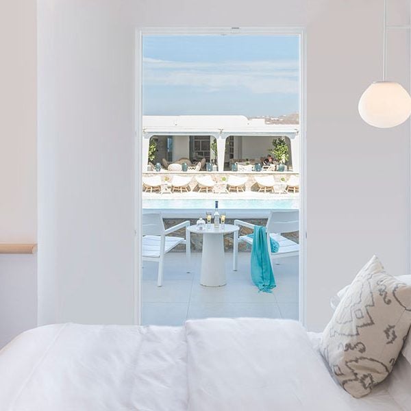 Luxurious white Cycladic suite with curved architectural lines overlooking azure Aegean Sea at golden sunrise, featuring minimalist design and private balcony