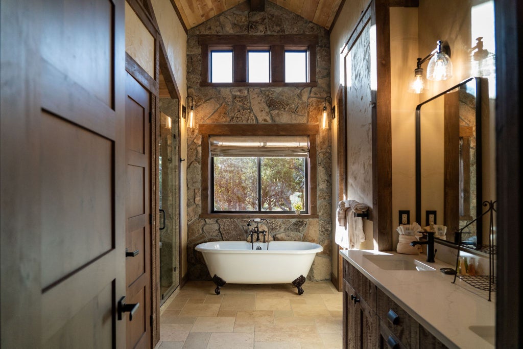 Rustic wooden lodge room with plush bedding, large windows overlooking scenic mountain landscape, warm earth tones, and elegant wilderness-inspired decor at Scenset Mountain Ranch