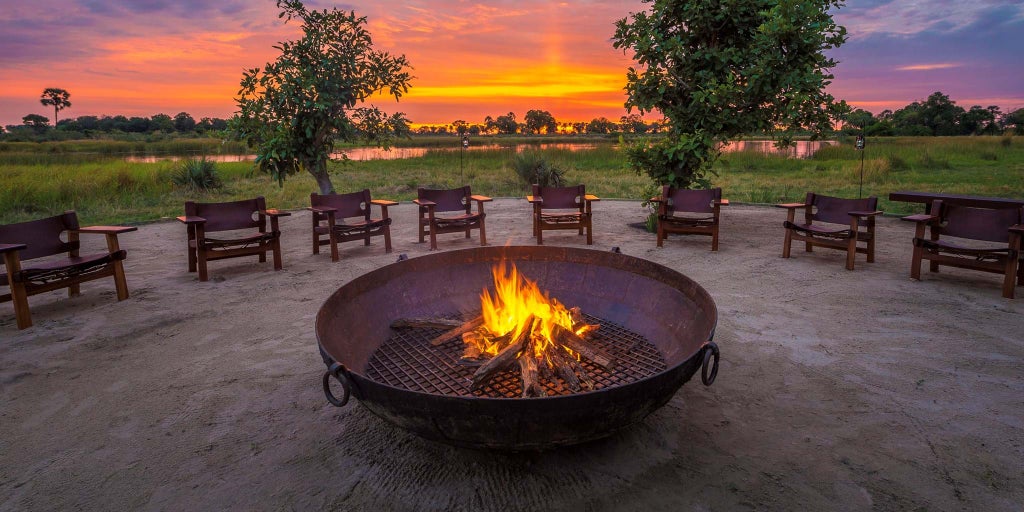 Elevated wooden safari lodge with private deck overlooking Okavango Delta wetlands, surrounded by acacia trees at sunset