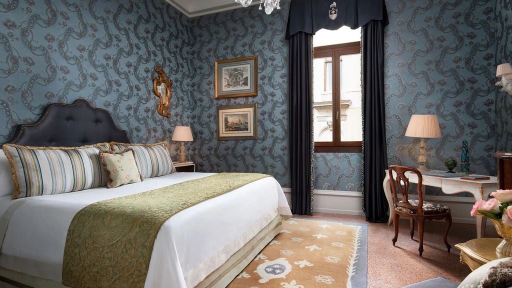 High-end hotel suite with ornate Venetian decor, crystal chandelier, gilded mirrors, antique furnishings and plush king bed with damask linens.