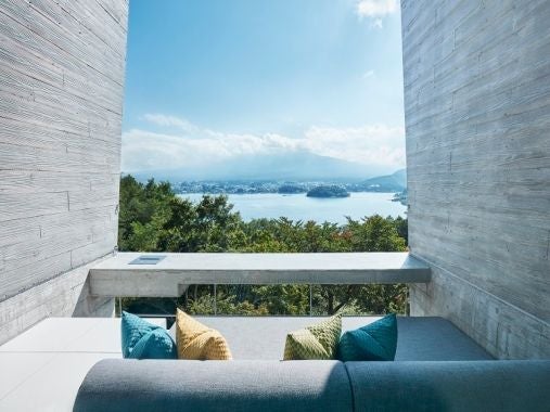 Modern luxury resort balcony with private wooden deck jutting over Mount Fuji's forested slopes, minimalist concrete design at dusk