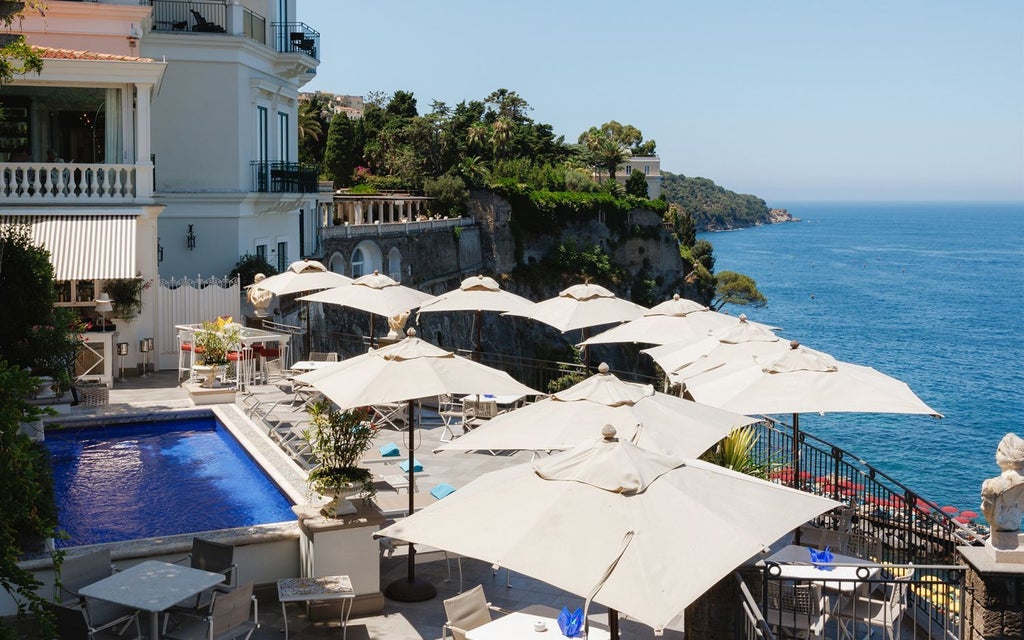 Luxurious coastal hotel Bellevue Syrene perched on Sorrento's cliffside, overlooking azure Mediterranean waters with elegant white architecture and lush green terraces