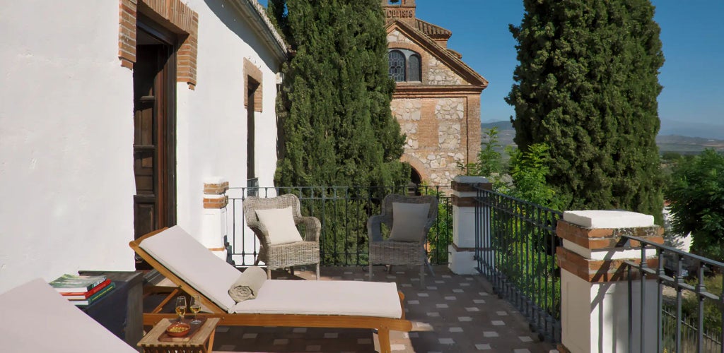 Elegant Spanish terrace with white-washed walls, rustic wooden furniture, and panoramic view of rolling countryside at luxurious Cortijo del Marqués