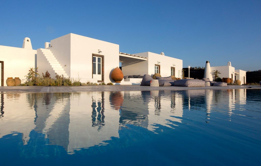 Infinity pool overlooking Santorini's caldera at sunset, with white sun loungers and minimal design terrace against blue sea views