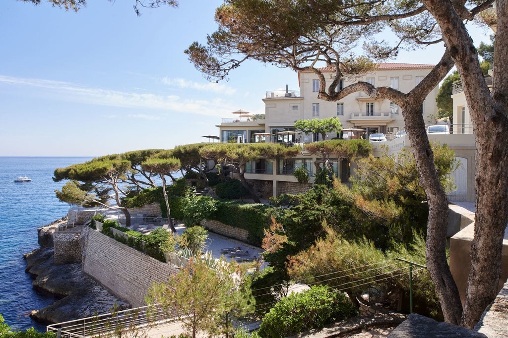 Elegant white Mediterranean hotel perched on cliffs overlooking azure sea, with terraced gardens and infinity pool near Cassis, France