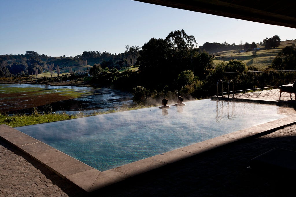 Modern wooden luxury hotel with floor-to-ceiling windows perched on coastal cliffside overlooking Pacific Ocean at sunset in Chile