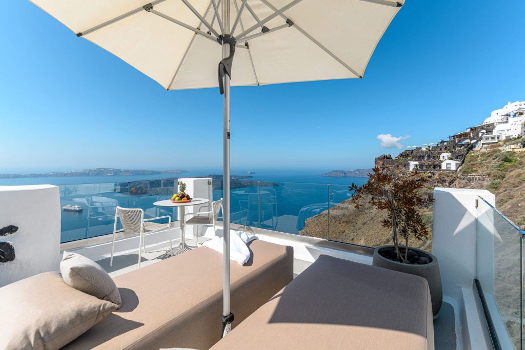 Luxurious white-washed cave suite with curved archways, blue sea view, and minimalist Cycladic design overlooking Santorini's stunning caldera landscape