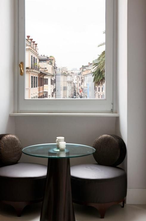 Opulent boutique hotel terrace with elegant white furnishings overlooking Rome's historic Piazza di Spagna, bathed in warm golden sunlight