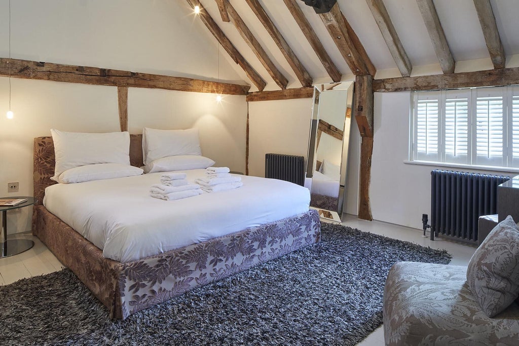 Elegant wooden-paneled bedroom with exposed beams, plush white bedding, and rustic charm in a converted mill room near scenic countryside