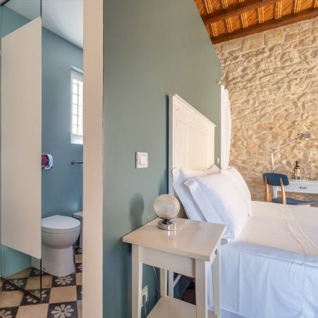 Elegant rustic suite at Casa Talía with exposed stone walls, minimalist decor, and warm terracotta tones overlooking scenic Italian landscape