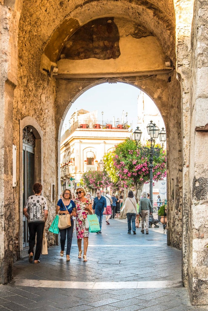 Cliffside ancient stone buildings of Taormina, Sicily, with Mount Etna's snow-capped peak rising majestically in the background