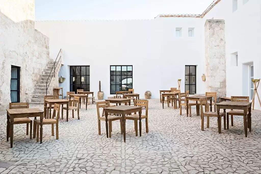 Rustic stone tower hotel with elegant arched windows, surrounded by Mediterranean gardens and a tranquil infinity pool at sunset