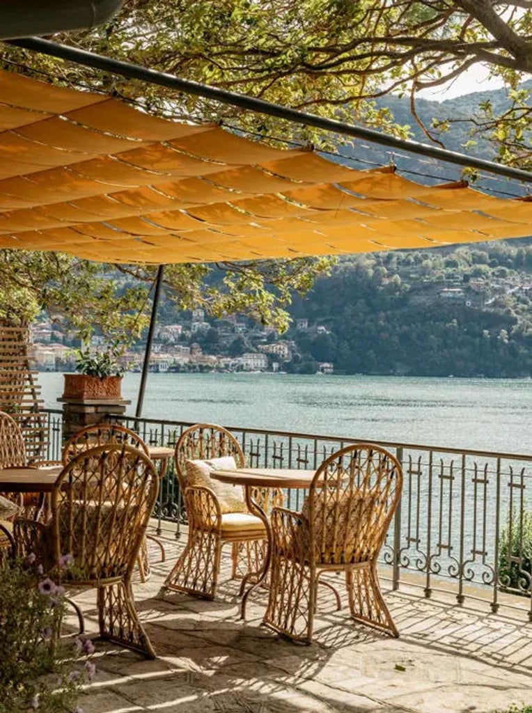 Elegant Italian lakeside villa with symmetrical stone facade, ornate balconies and manicured gardens overlooking Lake Como at sunset