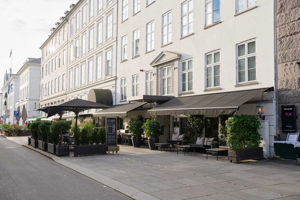 Elegant Danish hotel facade with white exterior, large windows, and classic architectural details, nestled in a charming urban street setting at scenset.