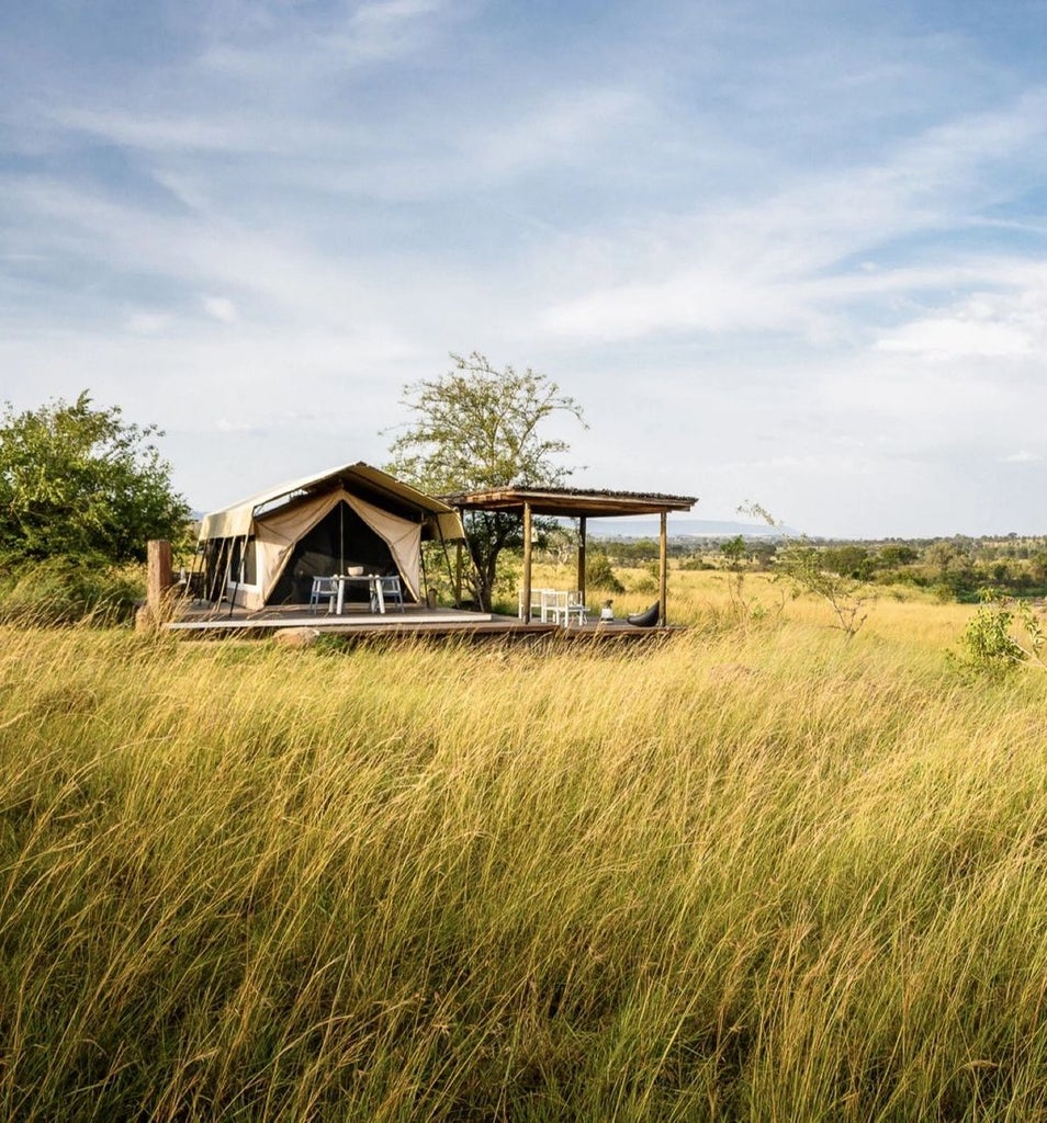 Elegant safari tent suite overlooking the Mara River, featuring canvas walls, private deck, and modern furnishings in natural tones