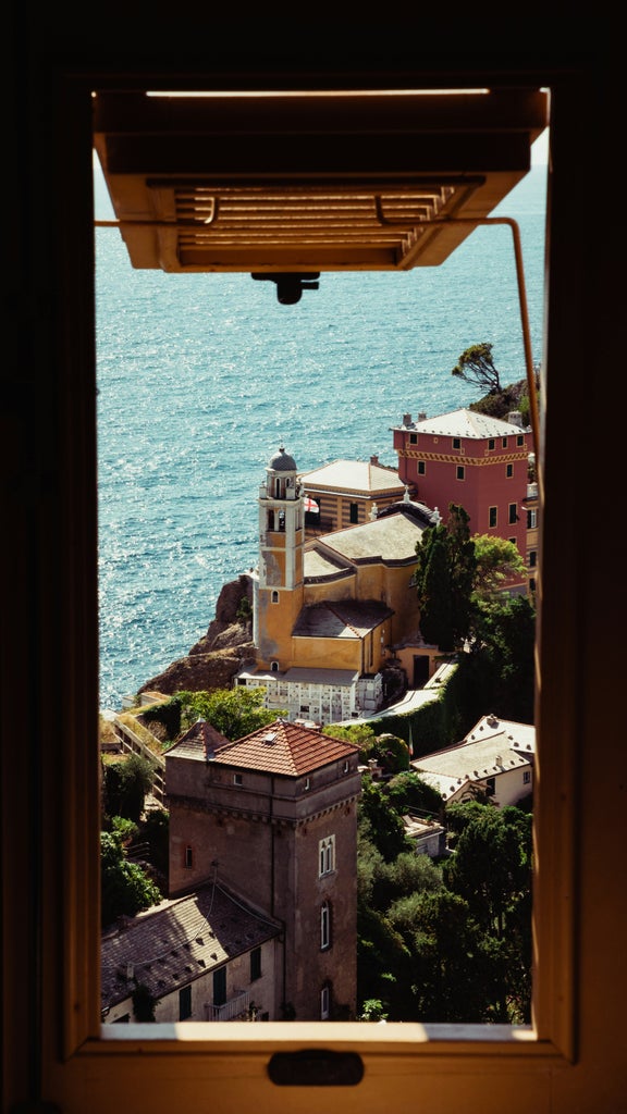 Colorful pastel buildings line Portofino's iconic harbor at sunset, with luxury yachts moored against a backdrop of Mediterranean cliffs