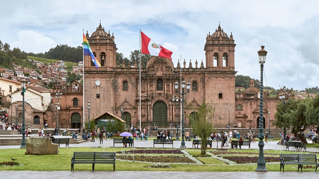 Historic Plaza de Armas in Cusco at sunset, with ornate Spanish colonial cathedral, illuminated palm trees and Andean mountains backdrop