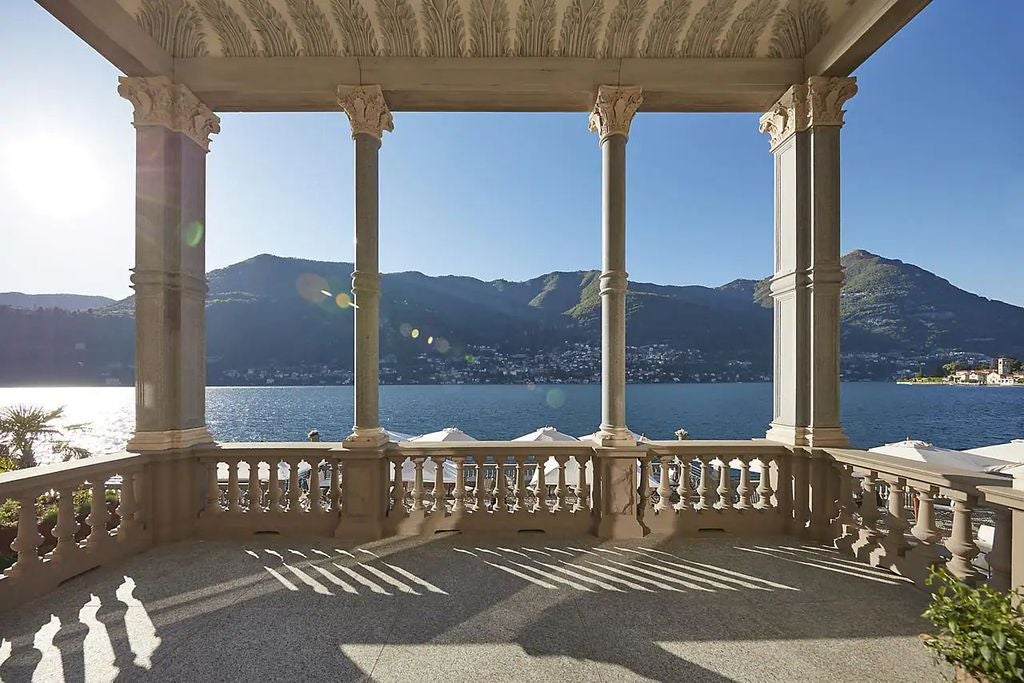 Elegant lakefront hotel with infinity pool overlooking Lake Como, framed by snow-capped mountains and Mediterranean gardens at sunset