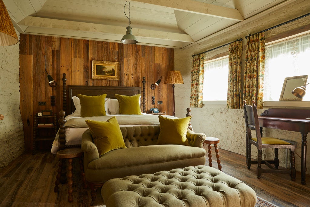 Luxurious hotel room with plush white bedding, rustic wooden furniture, and large windows overlooking lush green South Downs countryside landscape