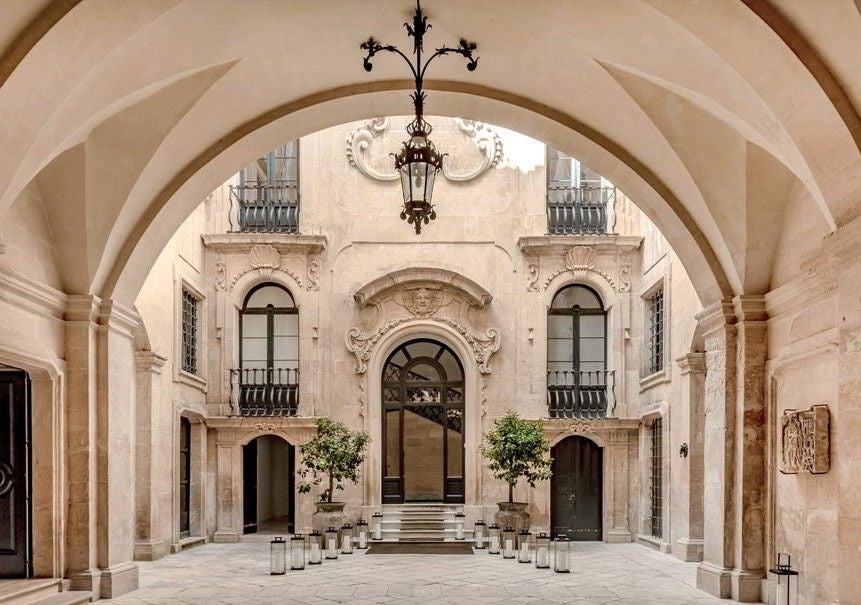 Elegant Italian palazzo hotel with ornate stone balconies, tall arched windows, and classical facade illuminated at dusk in warm lighting