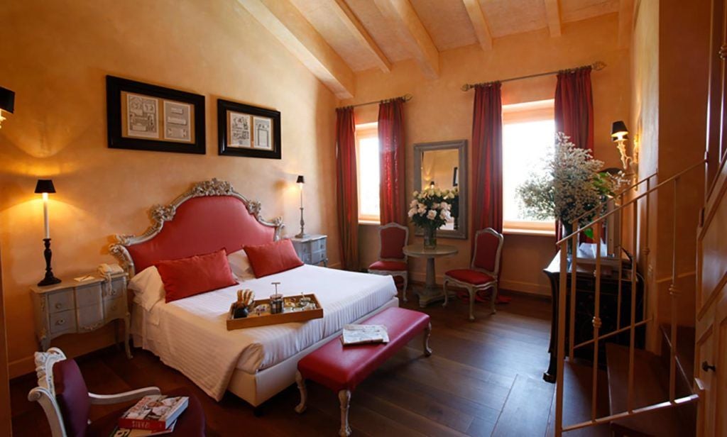 Elegant Superior room at L'Andana, Tuscany, featuring plush white linens, rustic wooden furnishings, and soft natural light streaming across refined Mediterranean decor