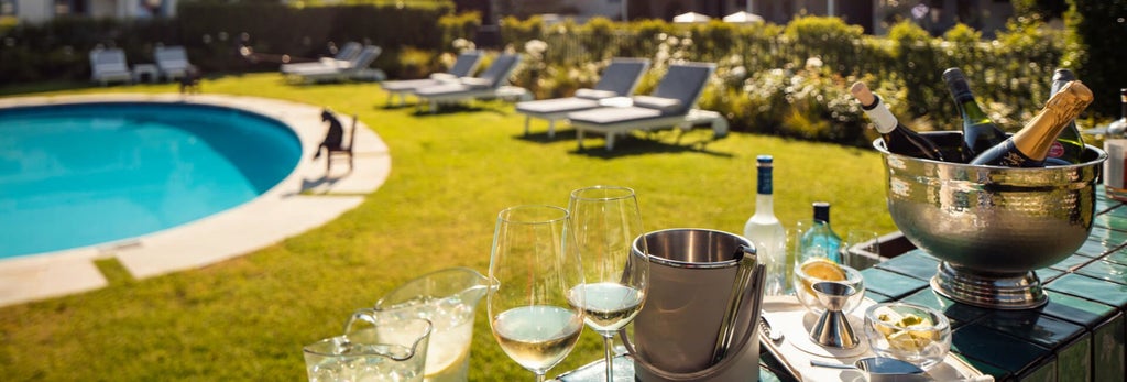 Luxurious pool suite with sun loungers, stone-tiled terrace, lush garden backdrop, and elegant outdoor swimming pool at Le Quartier Français resort