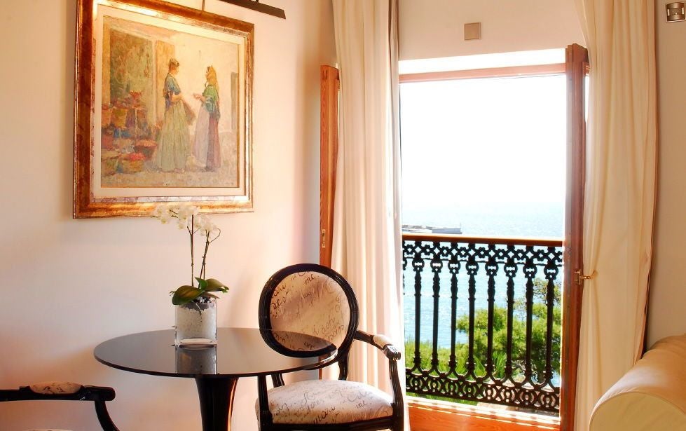 Elegant junior suite with white modern furnishings, expansive window overlooking historic Dalt Vila, featuring minimalist design and warm Mediterranean lighting