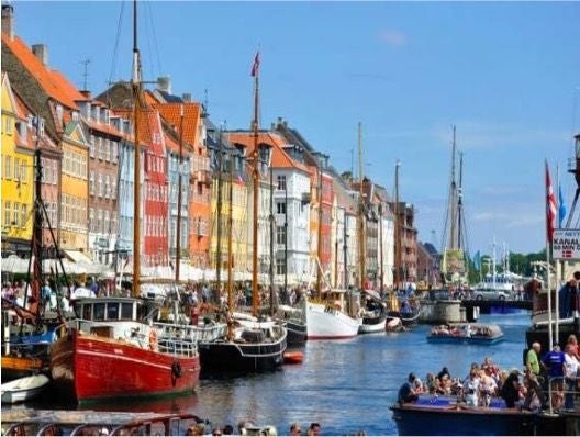 Elegant wooden boat gliding through Copenhagen's historic Grand Canal, with colorful waterfront buildings and ornate architectural details reflecting in tranquil waters.