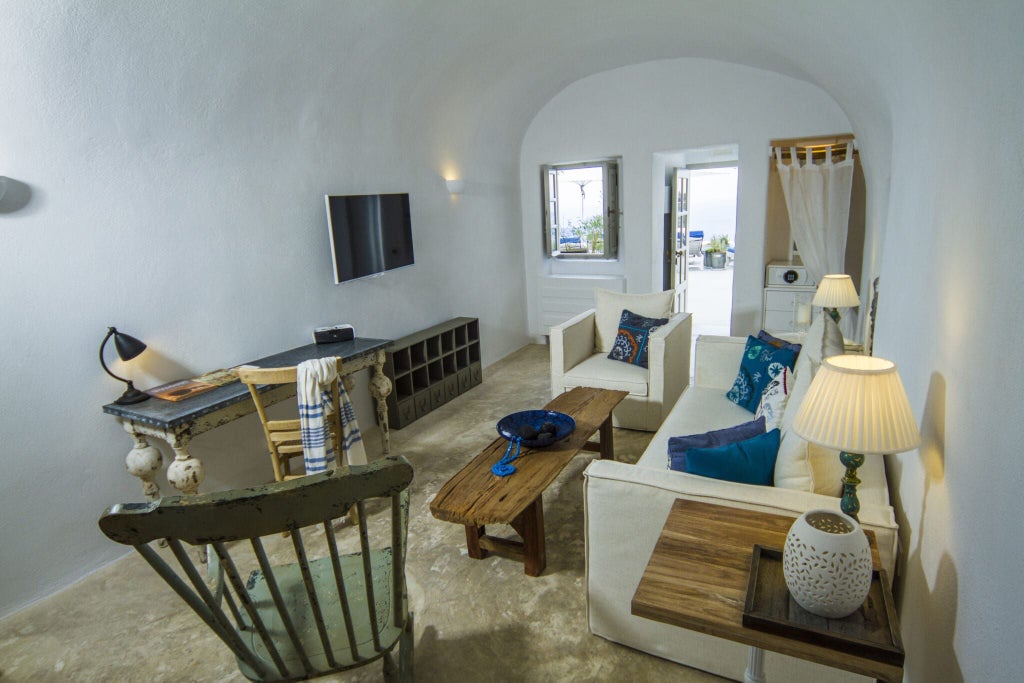 Luxurious white-washed cave suite in Santorini with curved arched ceilings, blue Aegean Sea view, and minimalist Cycladic architectural design