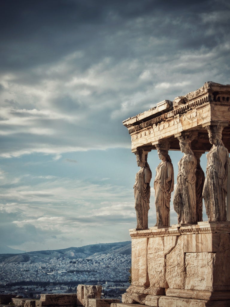 Majestic marble columns of the Parthenon atop the Acropolis hill glowing golden at sunset against a vibrant blue Athens sky