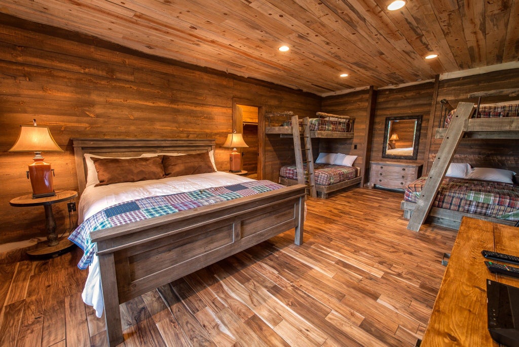 Rustic wooden lodge room with plush king bed, large windows overlooking mountain landscape, warm earth tones, and elegant wilderness-inspired decor at scenic ranch accommodation